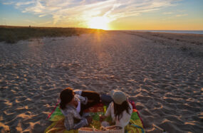 Two people relaxing on a beach blanket at sunset