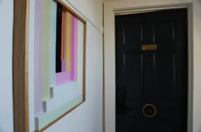 Hallway with colorful framed art and dark door at Mercury