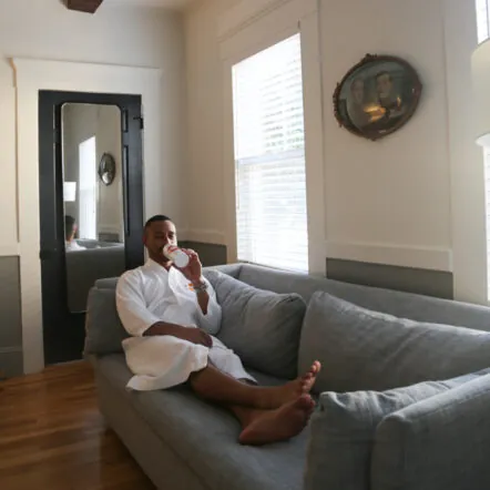 Guest in bathrobe njoying coffee on a gray sofa near window