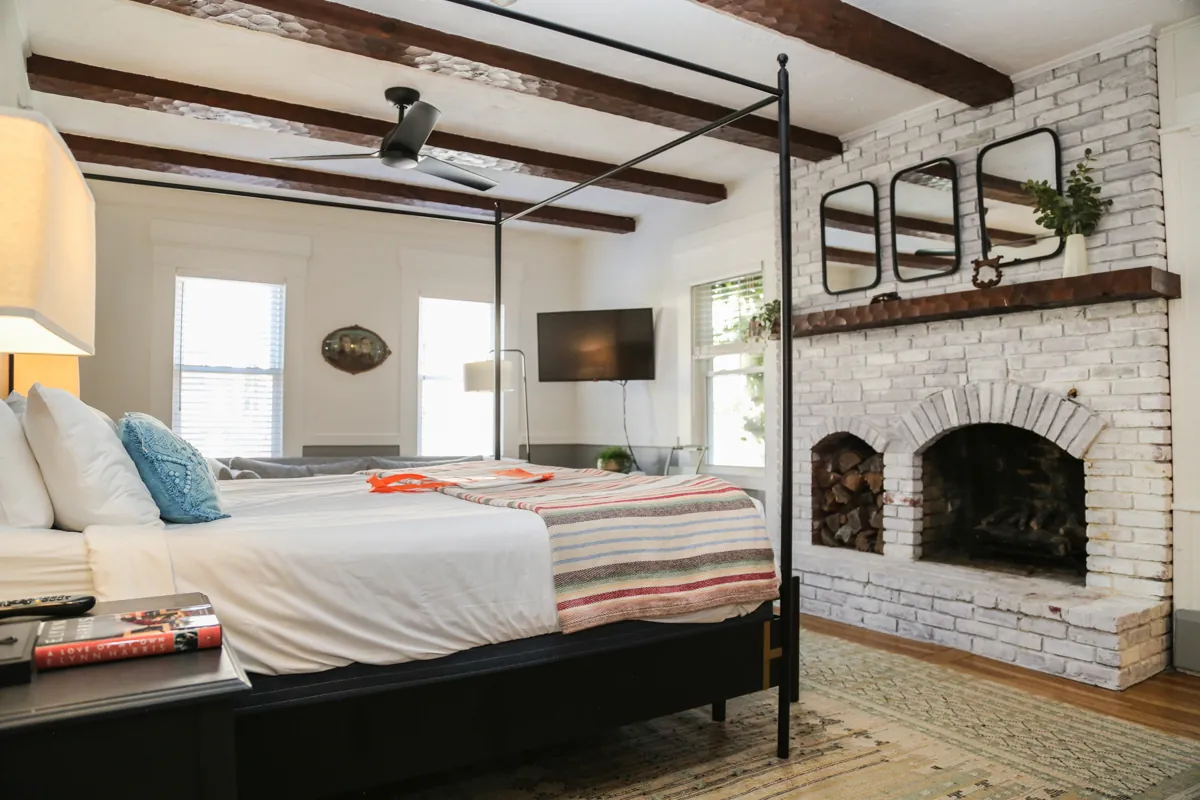 Cozy guest room with four poster bed, white brick fireplace and wooden ceiling beams